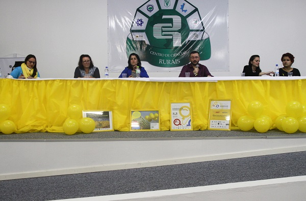Mesa-redonda do evento com os palestrantes sentados. Toda a ambientação traz a cor amarela em alusão ao mês