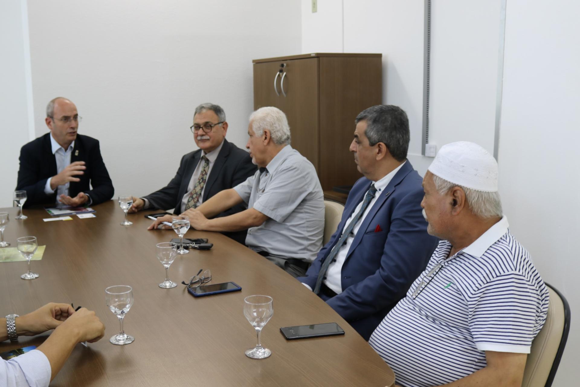 Foto horizontal de cinco homens sentados à mesa, no gabinete do reitor. Na ponta da mesa está o vice-reitor e do lado direito da imagem está a comitiva com quatro homens