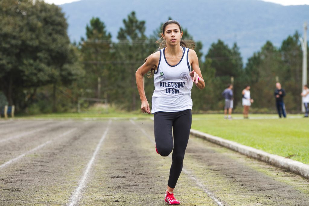 Em primeiro plano, atleta corre em pista de corrida.