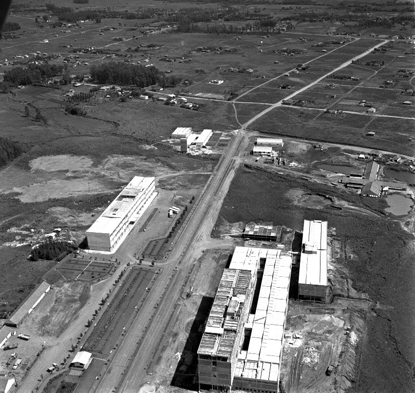 Fotografia quadrada preto e branca da vista aérea da Avenida Roraima. A esquerda, prédio do Colégio Técnico Industrial e do Centro de Tecnologia, a direita prédio do Hospital Universitário de Santa Maria, ao fundo campo com vegetação.