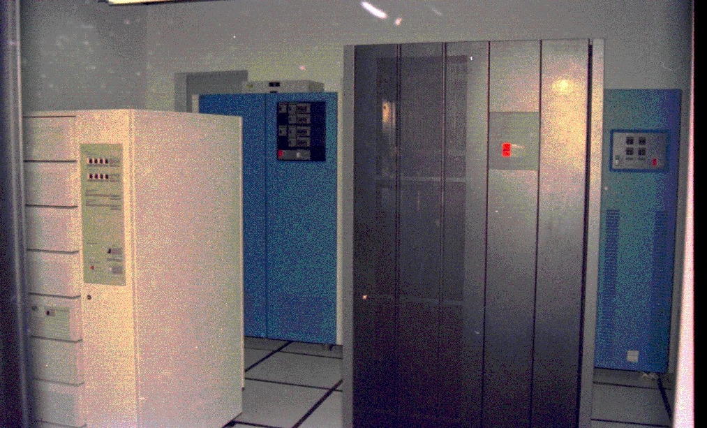 Fotografia horizontal colorida da Inauguração do Computador CPD IBM 9672. Em uma área interna, 4 computadores, a esquerda um branco e atrás dele um azul. A direita, um prata e atrás dele outro azul.