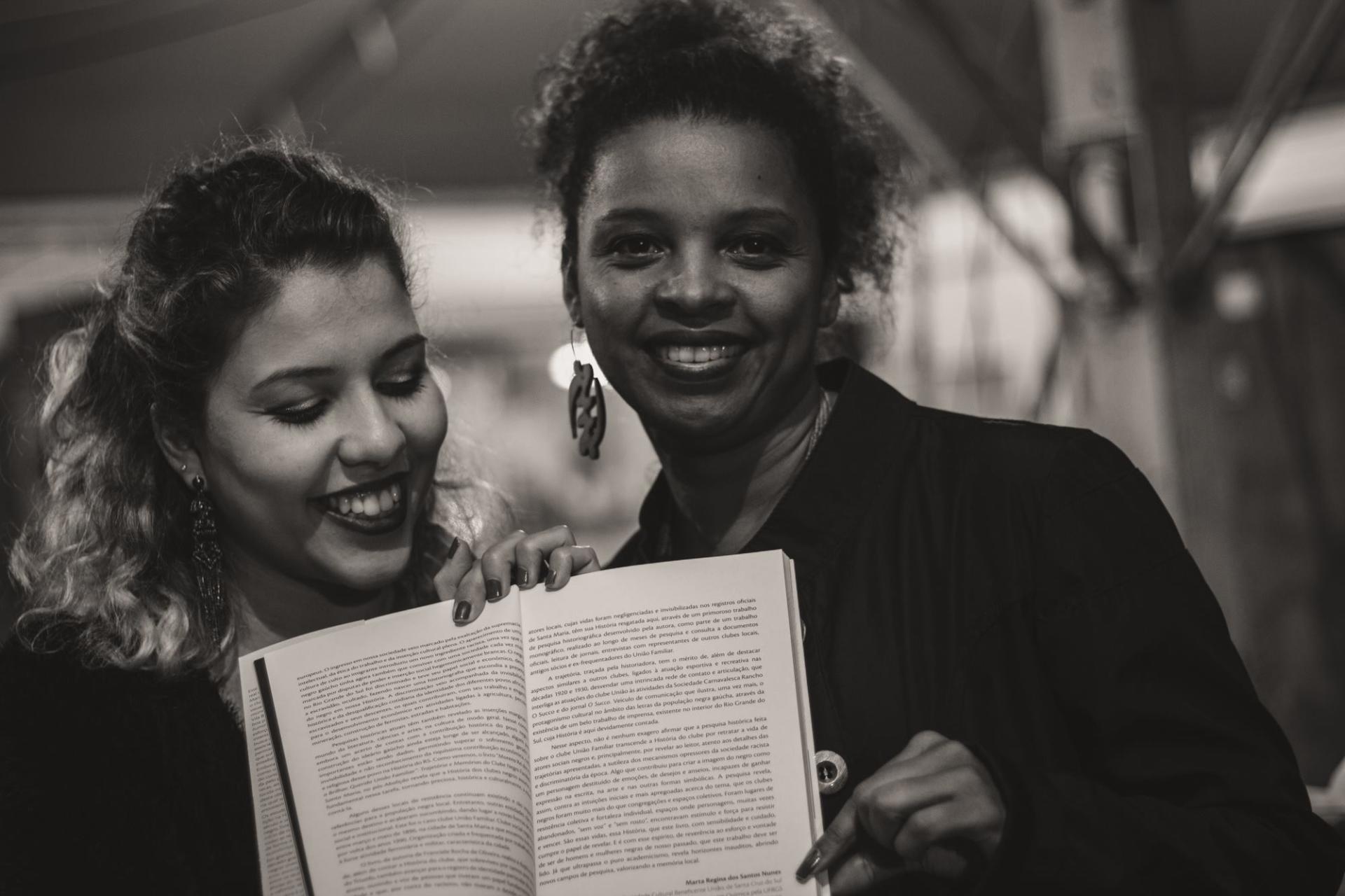 Foto preto e branco de duas mulheres segurando um livro aberto