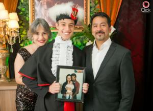 Foto colorida de um rapaz com toga de formatura com uma mulher à esquerda e um homem à direita