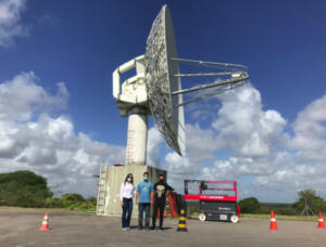 Membros da equipe Rocket Lab posam ao lado da enorme antena de telemetria do CLBI.