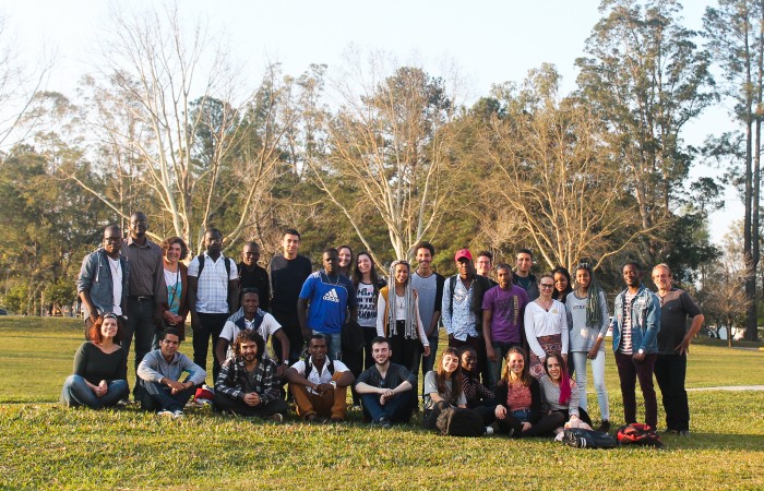 Cerca de vinte estudantes refugiados posam com professores do projeto MIGRAIDH no bosque da UFSM