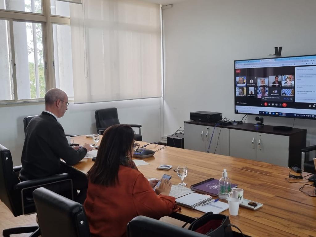 Reitor Luciano Schuch e vice-reitora Martha Adaime sentados em uma mesa de madeira, de frente para um monitor que transmite os demais conselheiros