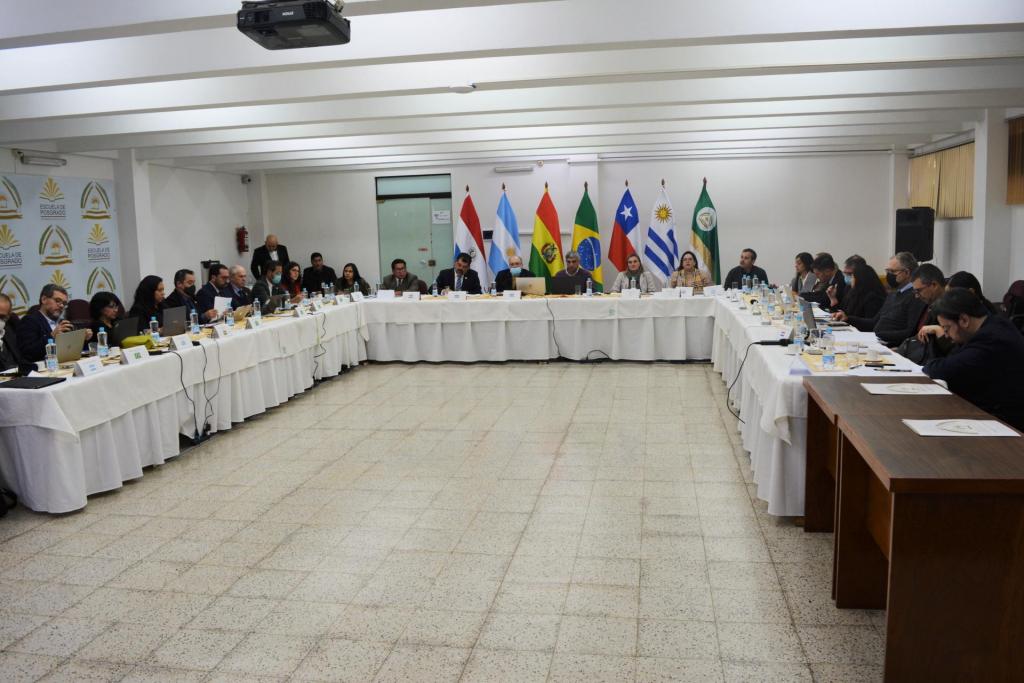 Grande mesa em formato de U, onde todos os delegados estão sentados. Atrás, ao centro, as bandeiras de paraguai, argentina, brasil, chile e Uruguai