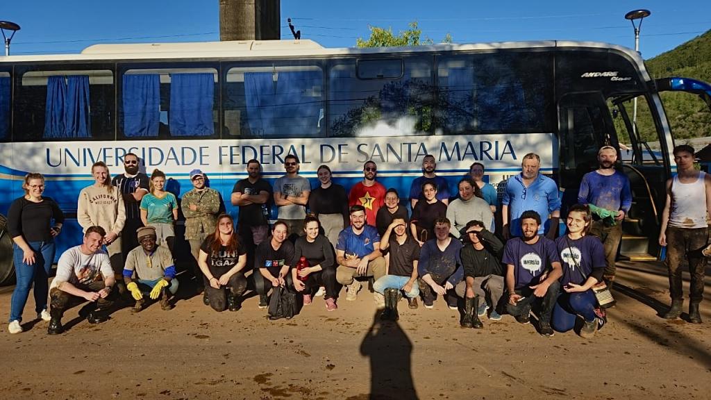 foto colorida horizontal com um ônibus da UFSM estacionado e ao lado dele várias pessoas em pose para foto, alguns agachados e outros em pé