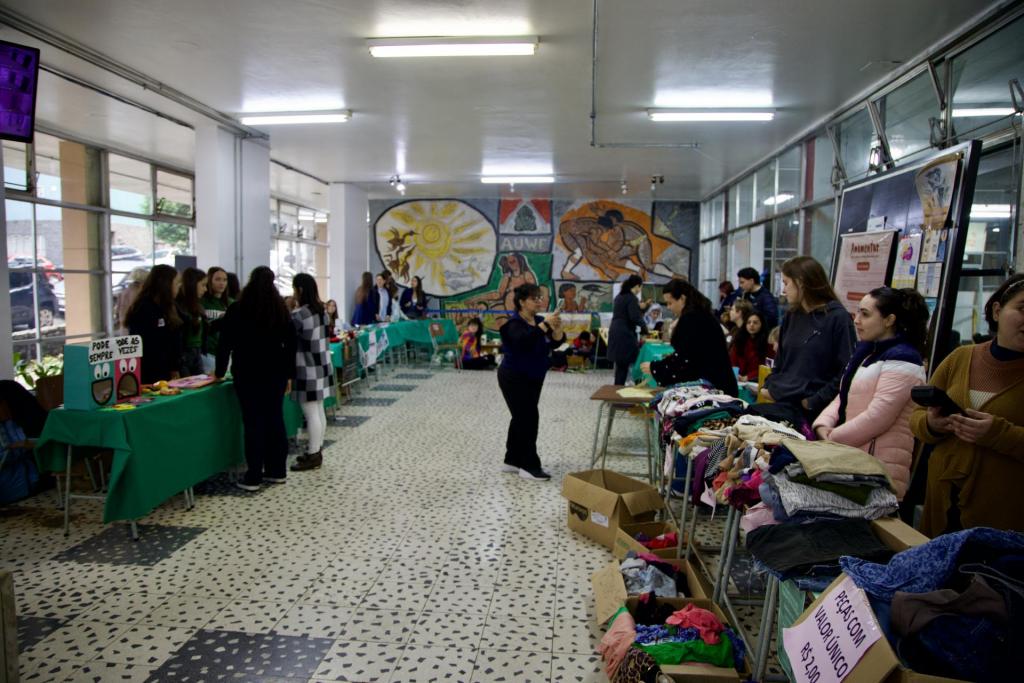 Foto colorida horizontal. Dos lados direito e esquerdo estão duas fileiras de pessoas em estandes, com itens em exposição, como peças de roupas coloridas.