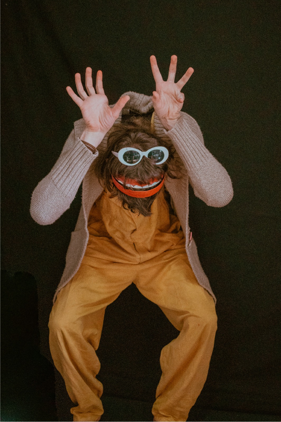 Foto colorida vertical de pessoa vestida com máscara peluda com óculos e com as duas mãos à cabeça