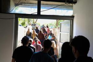 Foto horizontal. Um grupo de pessoas, fotografadas de costas, sobe uma rampa que os conduz do subsolo até o estacionamento da Reitoria.