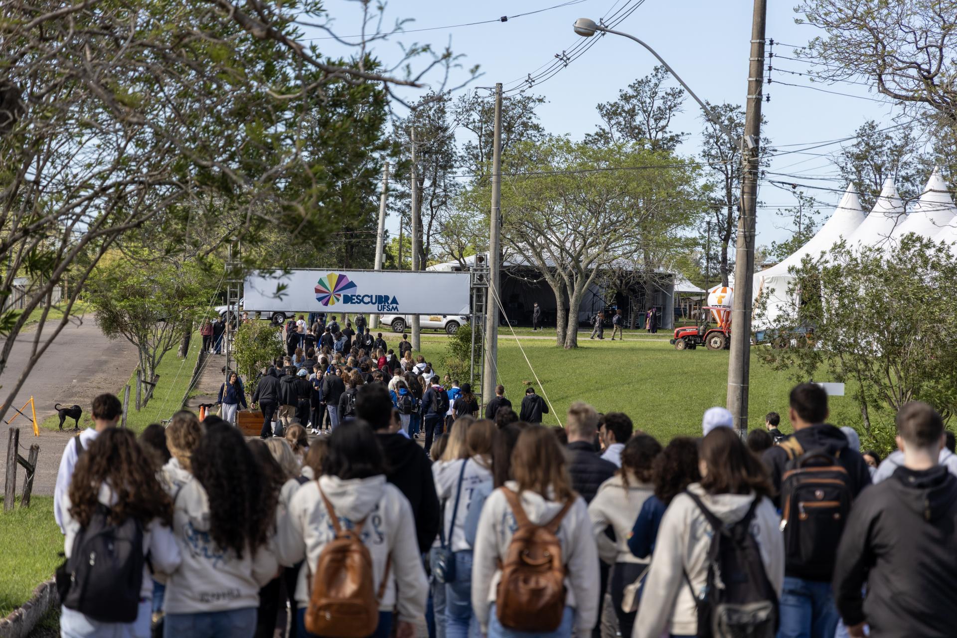 Foto horizontal e colorida de um grupo de estudantes caminhando em direção a ao pórtico de entrada do Descubra 2025