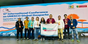 Foto colorida de nove pessoas lado a lado, com uma bandeira a frente escrito Geoparque Quarta Colônia