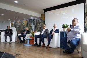 Fotosgrafia horizontal colorida com cinco homens sentados, um deles com microfone falando