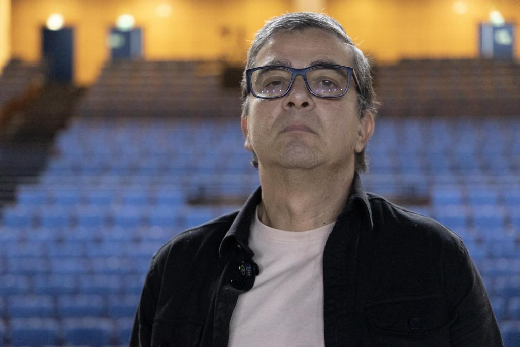 Foto colorida horizontal de Felipe, um senhor de óculo e cabelo prateado, á frente da arquibanca do Centro de Convenções.
