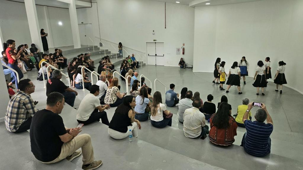 Foto colorida horizontal de grupo de pessoas sentadas em uma escadaria circular que preenche boa parte do espaço