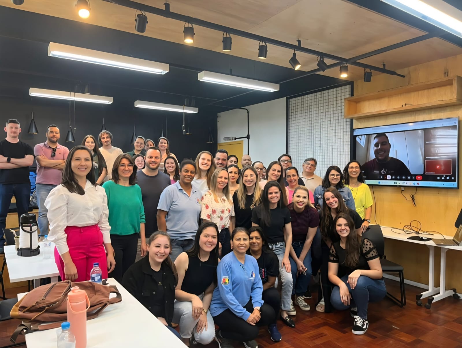 Foto colorida horizontal de grupo de pessoas sentadas em pé. O grupo é formado por homens e mulheres que vestem roupas mais formais ou casuais