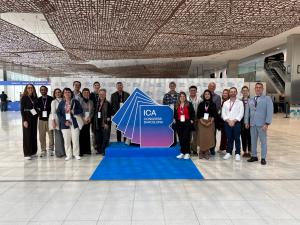 Foto horizontal. 18 pessoas estão em pé ao lado de um grande display com a logomarca do congresso.