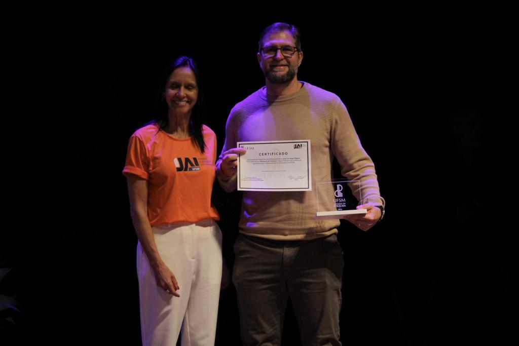 Foto colorida horizontal do professor Roger Wagner, destaque de Pesquisa, recebendo o prêmio da professora Cristina Nogueira