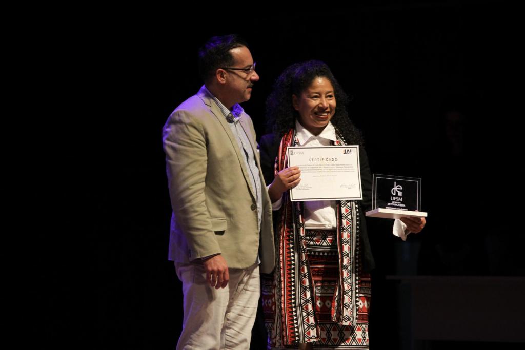 Foto colorida horizontal de Cátia Dutra recebendo a premiação do pró-reitor Flavi