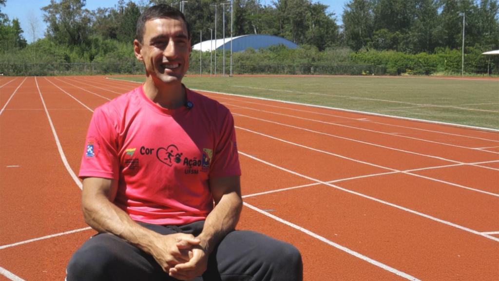 Foto colorida horizontal de Wagner, homem jovem. Ele está sentando do lado esquerdo. Atrás dele, a pista olímpica do CEFD, que tem um piso cor de telha com marcações em branco.