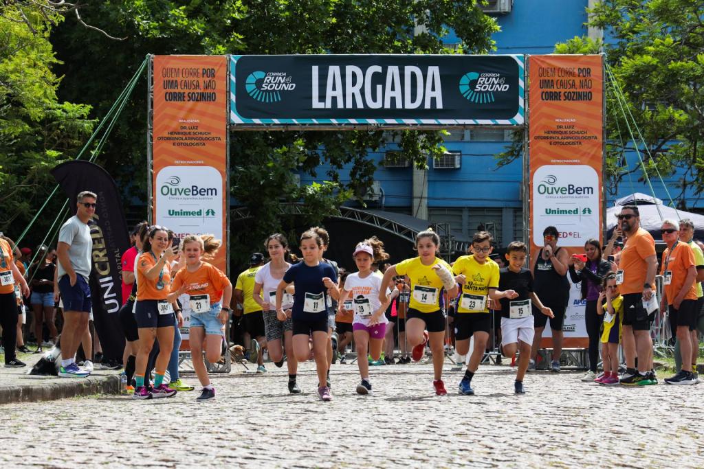 foto colorida horizontal de crianças correndo tendo uma estrutura escrito "largada"