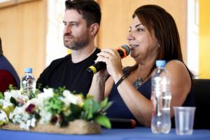 Foto horizontal e colorida de Martha Adaime segurando um microfone.