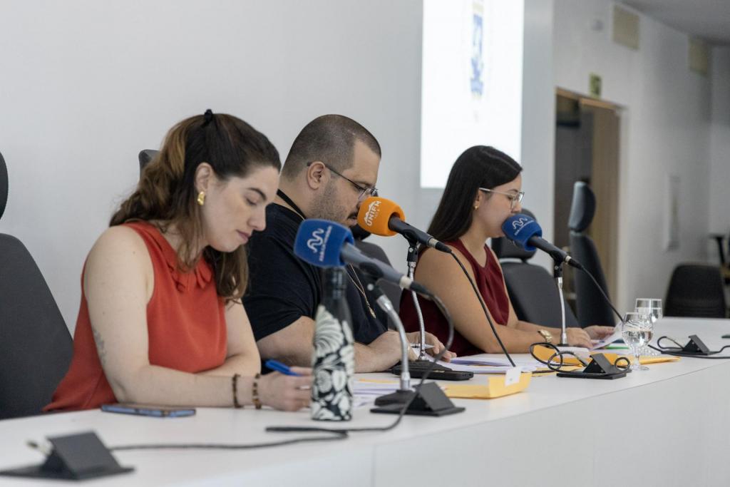Foto horizontal e colorida e duas mulheres e um homem lendo os nome dos aprovados em microfones.