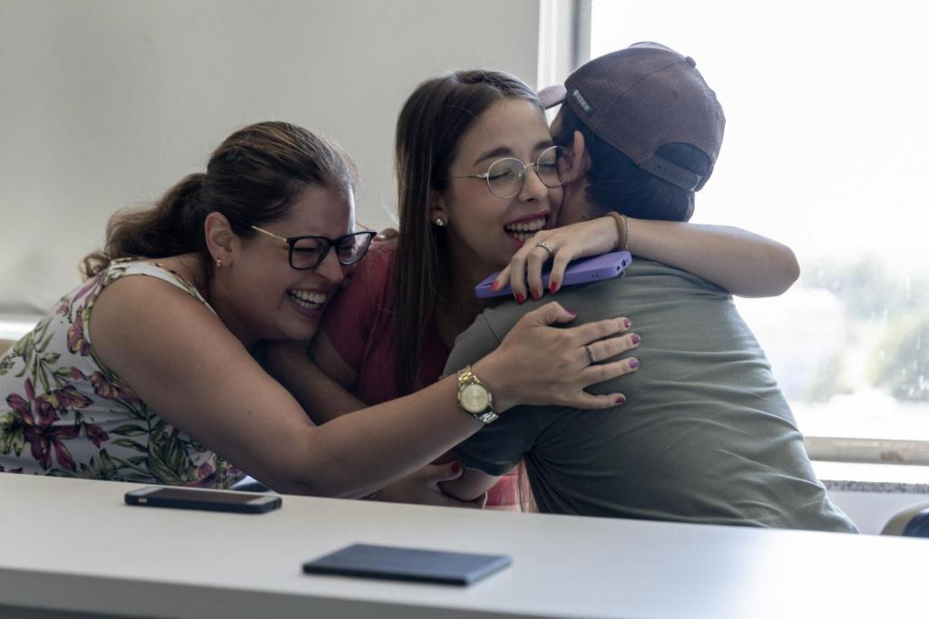Foto horizontal e colorida de mãe, filha e pai se abraçando e comemorando sentados.