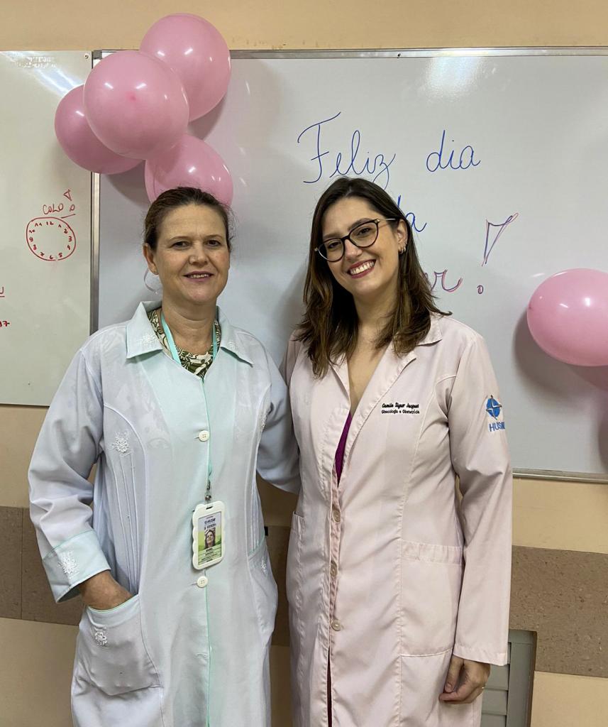 Foto colorida na vertical exibindo Izabel Cristina Hoffman, a esquerda, e Camila Jacques, a direita. As duas estão localizadas no setor de ginecologia do HUSM para realizar a aplicação do Implanon nas pacientes. 