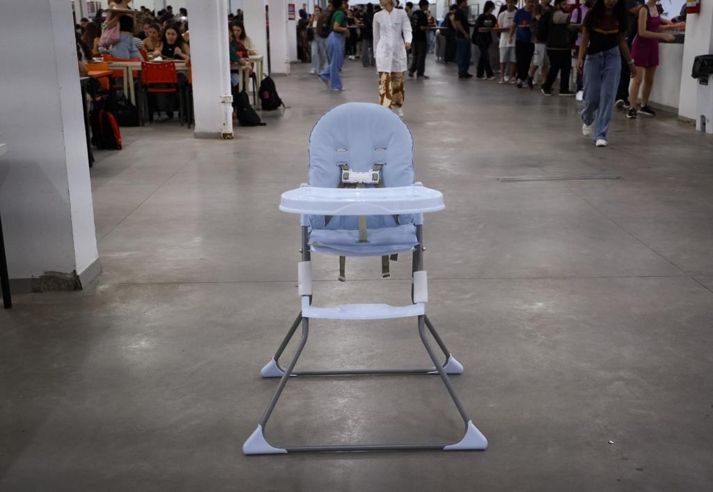 Foto colorida, horizontal. Em destaque, no centro da imagem, uma cadeirinha de alimentação infantil