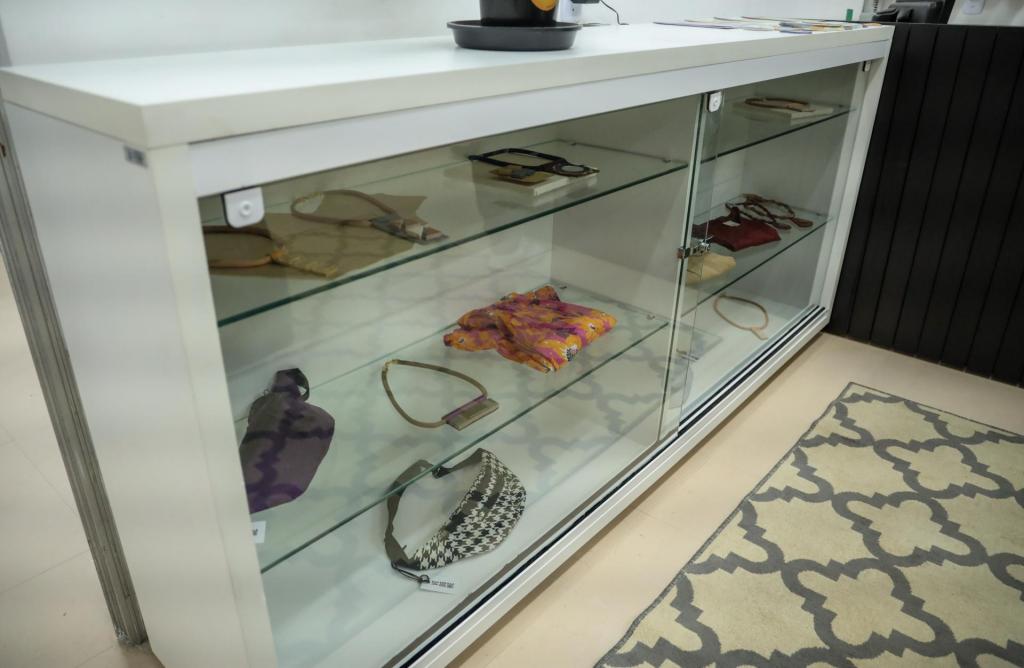 A foto mostra uma estante na qual estão expostos peças de vestuário, pochetes e colares.