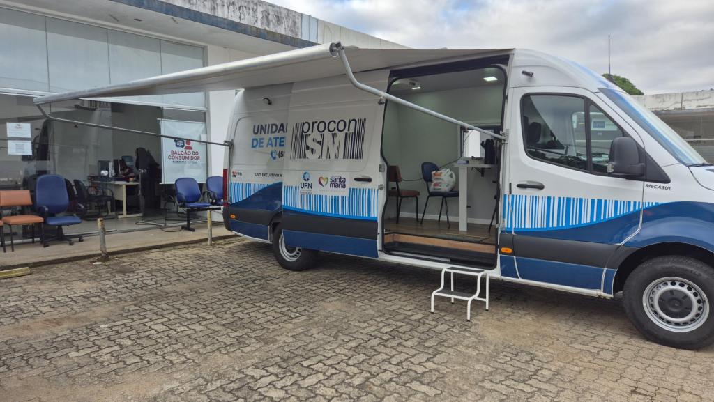 A foto mostra uma van estacionada em frente à sede do projeto Balcão do Consumidor, no centro comercial do campus sede da UFSM. O veículo é a unidade móvel do Procon de Santa Maria.