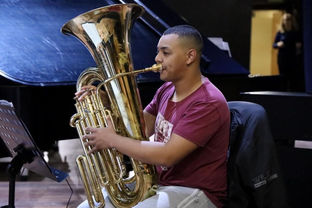 Alisson está sentado e tocando uma tuba, um grande instrumento de sopro. Ele está no Centro de Convenções 