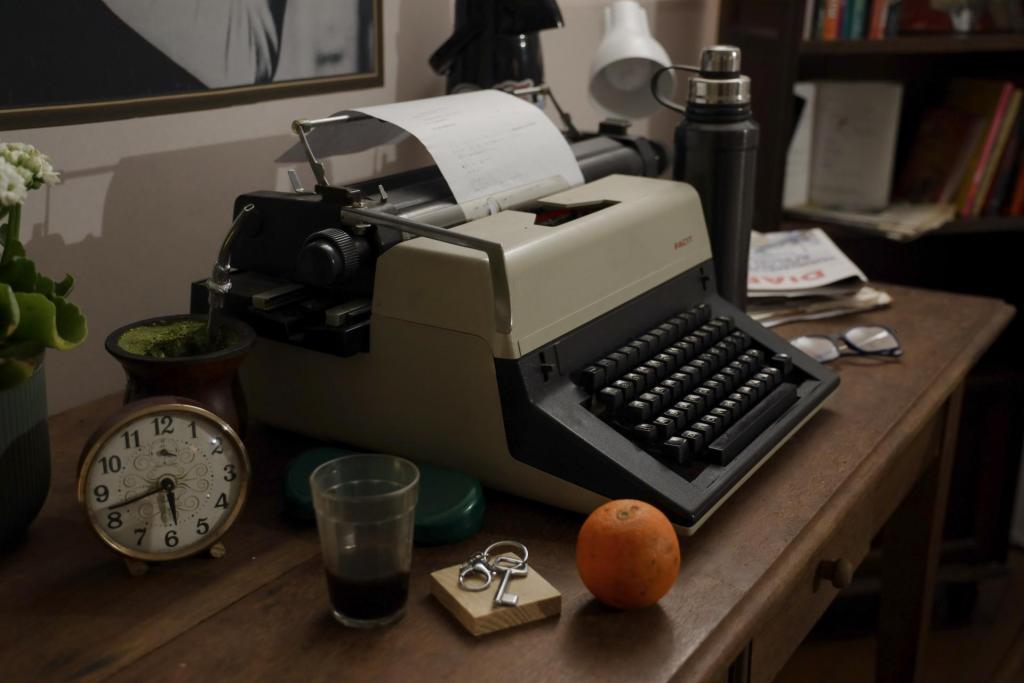 Foto colorida horizontal de uma mesa de trabalho com uma máquina de escrever com uma folha parcialmente escrita. Ao lado, um relógio, uma bergamota, um chimarrão, copo de café pela metade, uma térmica, um óculos redondo, um jornal dobrado. Mais ao lado, uma estante cheia de livros