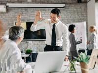 Two businessmen congratulating to each other on successful job and giving high-five. Focus is on young businessman.