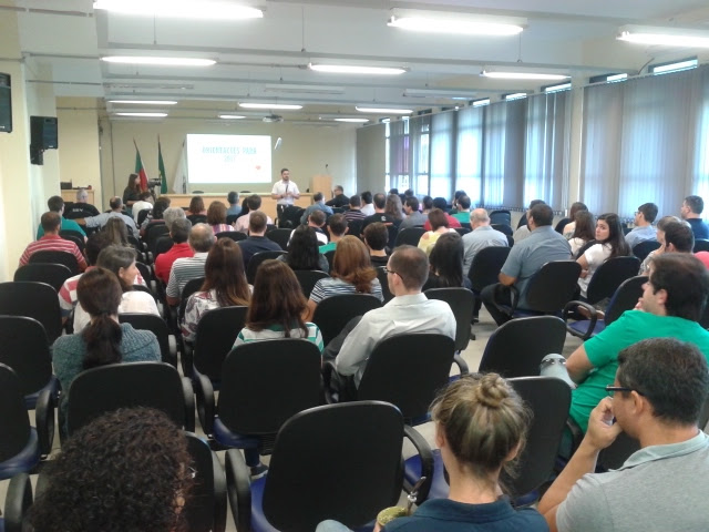 Pessoas sentadas em um auditório assistindo a uma apresentação de trabalho.