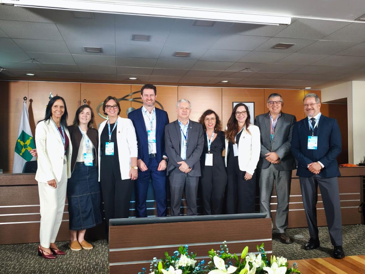 Registro fotográfico com a presença de oito representantes da proposta coordenada pela UNB. Ambos estão posicionados de pé, um ao lado do outro. Em meio a eles, os professores Tiago Bandeira Marchesan (Vice-Reitor) e Cristina Wayne Nogueira (Pró-Reitora de Pós-Graduação e Pesquisa). O registro foi feito no auditório da CAPES, um ambiente em tons marrons amadeirados presente na parede ao fundo e nos elementos que compõem a sala. No chão um carpete cinza. No fundo da foto, um painel de madeira com a logo da CAPES no centro, em composição com as bandeiras de Brasília, do Brasil e da CAPES, nesta sequência, localizadas no canto esquerdo.
