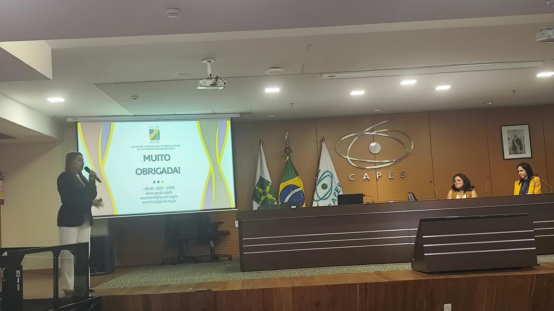 Plenária com apresentação da professora Rossana Valéria de Souza e Silva sobre internacionalização da pós-graduação brasileira, compondo a mesa de autoridades as professoras Cristina Wayne Nogueira e Kelly Castro. Em um auditório, com fundo de madeira, e logo da CAPES.