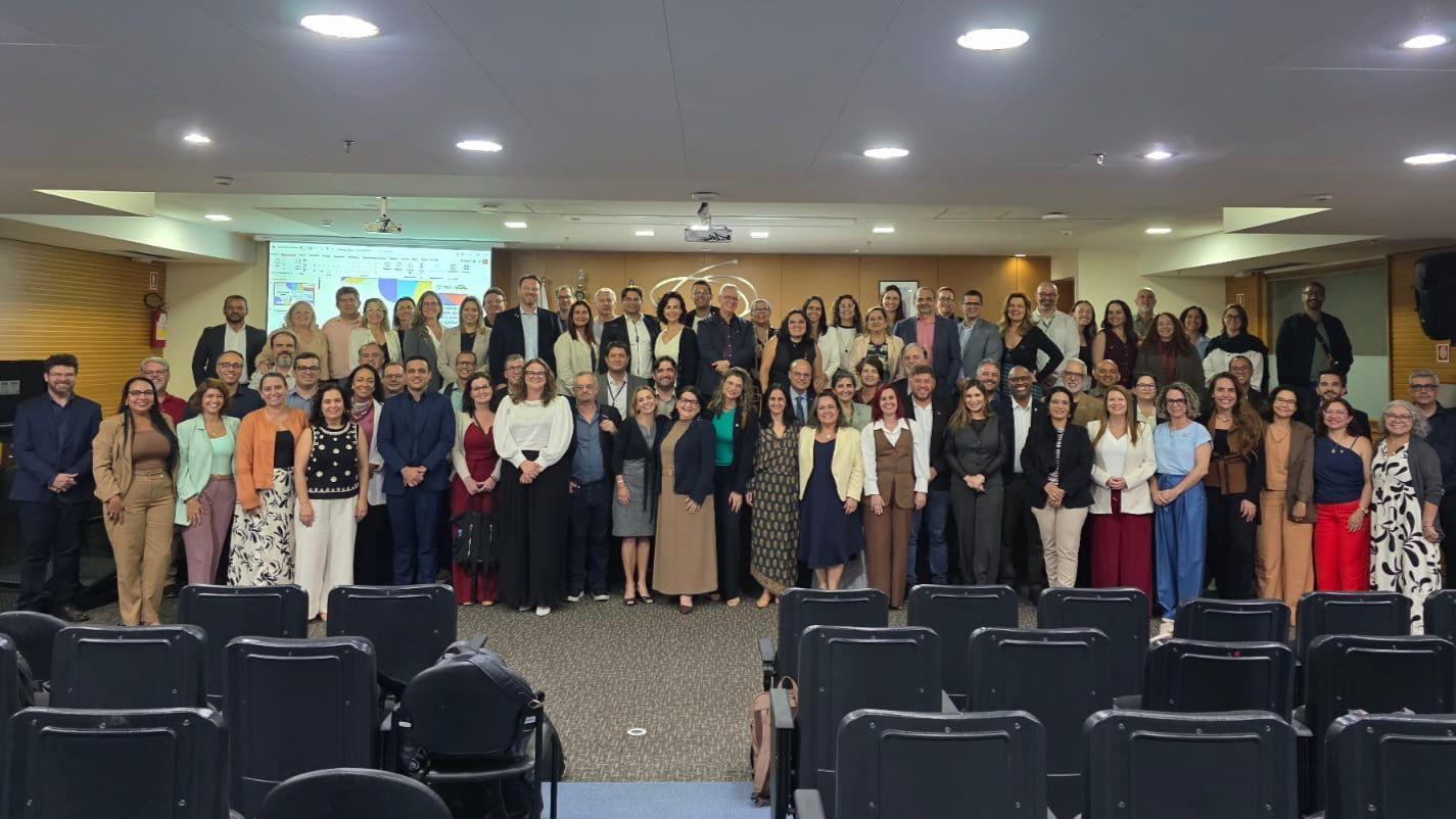 Fotografia com os representantes das universidades e instituições públicas. Em um auditório, com fundo de madeira, e logo da CAPES.