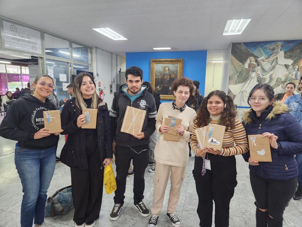 Seis pessoas, cada uma segurando um livro embalado para presente, no saguão da Biblioteca Central.