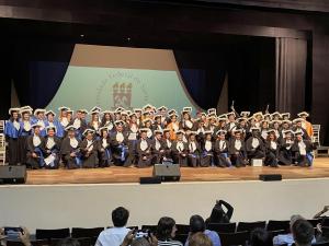 Foto retangular do palco do Centro de Convenções com os formandos, autoridades e homenageados posando em frente à mesa de honra para a foto oficial do evento 