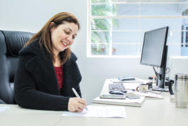 Mulher sentada escreve em papel sobre uma mesa.