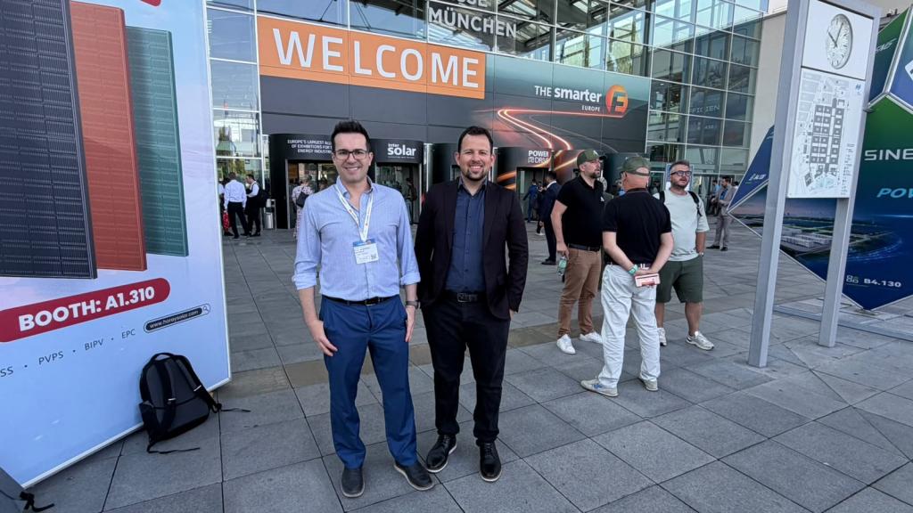 O professor Leandro Michels e o doutorando Anderson Severo posam em frente à entrada da Intersolar Europe 2026, em Munique, na Alemanha. Ao fundo aparecem o acesso ao evento e visitantes circulando pelo local.