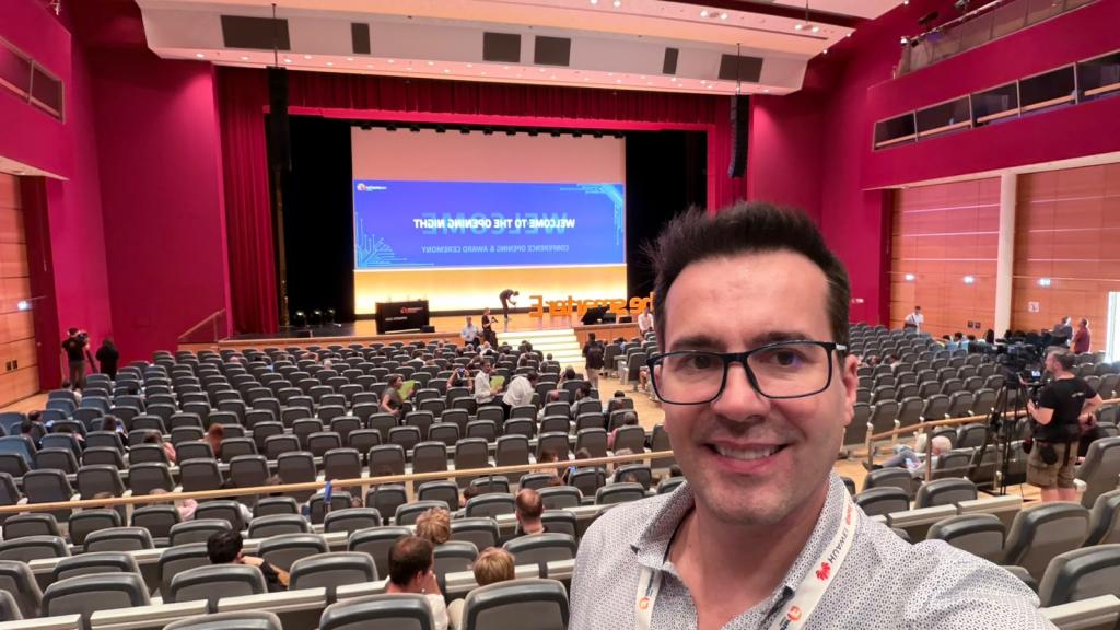Professor Leandro Michels faz uma selfie em um auditório da Intersolar Europe 2026, em Munique, na Alemanha. Ao fundo, há um palco com telão de uma sessão técnica e participantes ocupando parte da plateia.