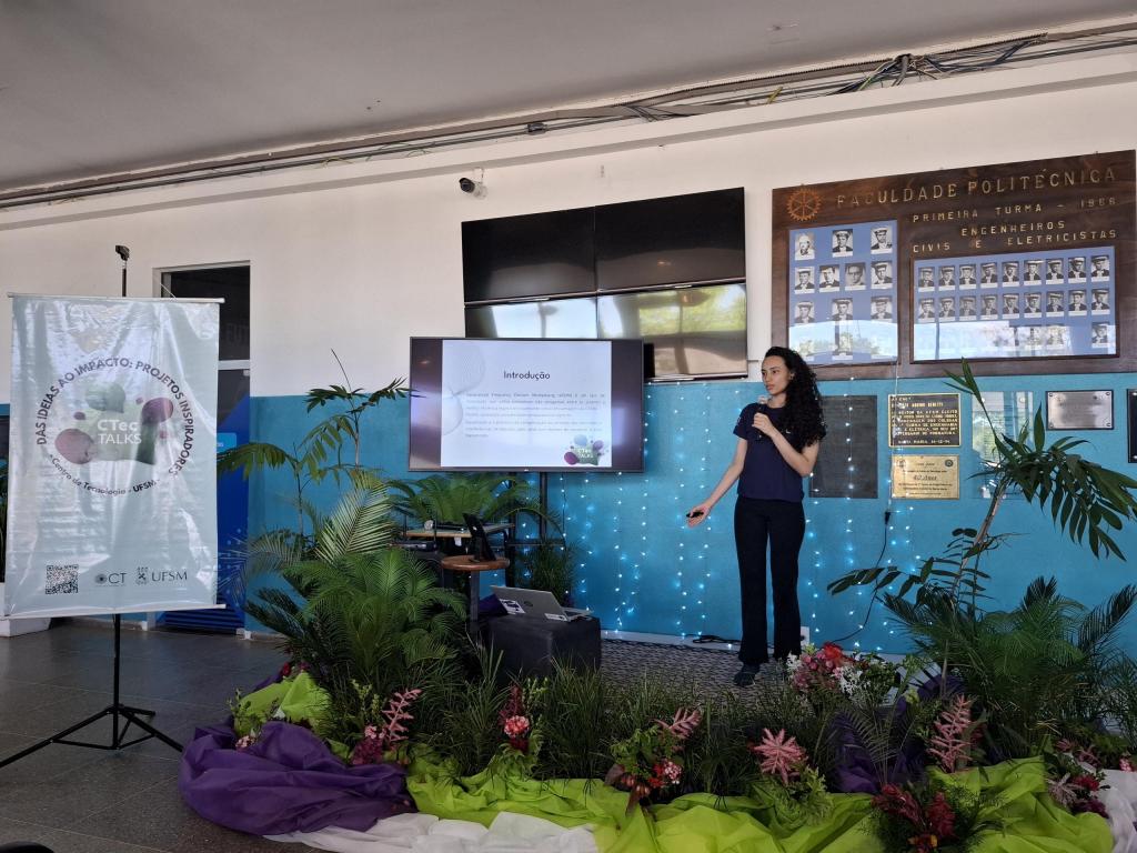 Pessoa apresenta projeto em tela durante o CTec Talks, em espaço decorado no Centro de Tecnologia da UFSM.