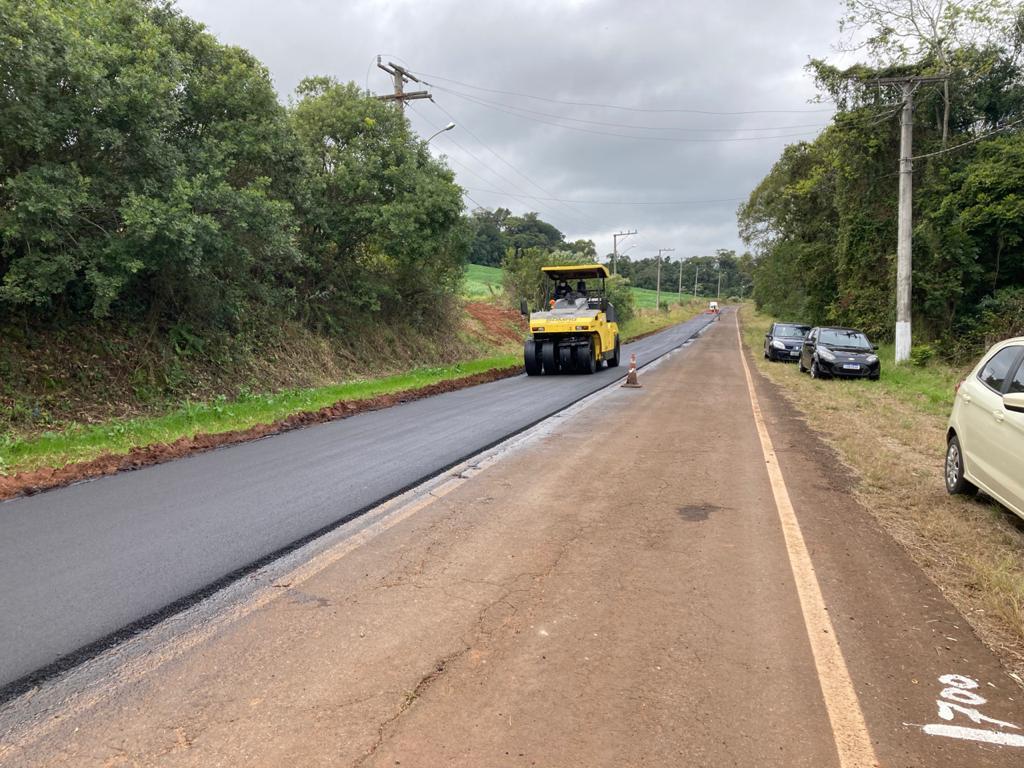 Imagem do trecho de acesso à UFSM-FW. Aparecem na imagem, à direita, parte da estrada com asfalto antigo, e à esquerda, máquina realizando trabalho na massa asfáltica recém colocada.