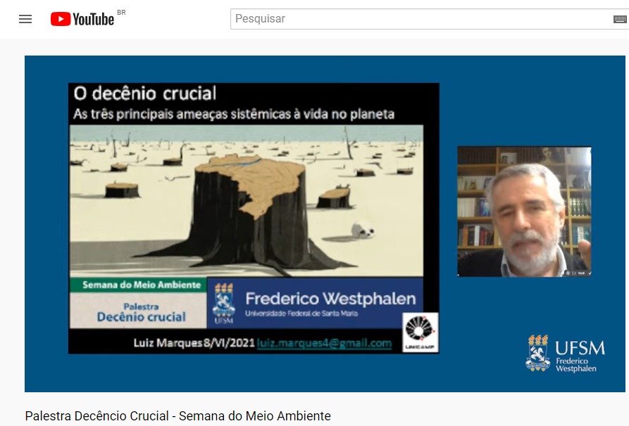 Print de tela com a apresentação da palestra "Decênio crucial", ministrada pelo Prof. Dr. Luiz Marques, da Unicamp, em comemoração à Semana do Meio Ambiente. Aparecem na imagem o Prof. Dr. Luiz Marques à direita, e ao centro a imagem com os dizeres: O decênio crucial - As três ameaças sistêmicas à vida no planeta.