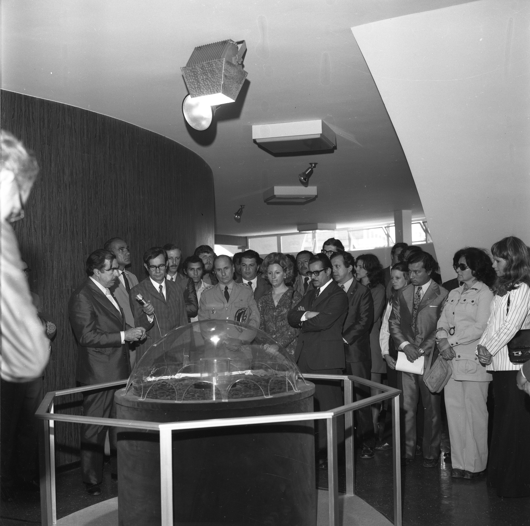Foto preto e branca de diversas pessoas no hall do Planetário em torno de uma mesa de exposição