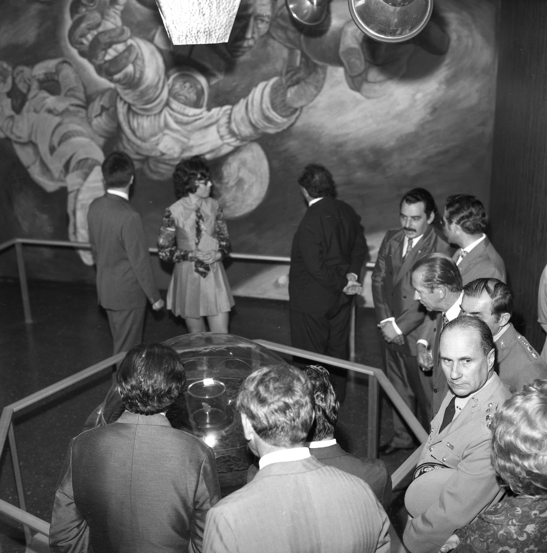 Foto preto e branca de diversas pessoas no hall do Planetário em torno de uma mesa de exposição